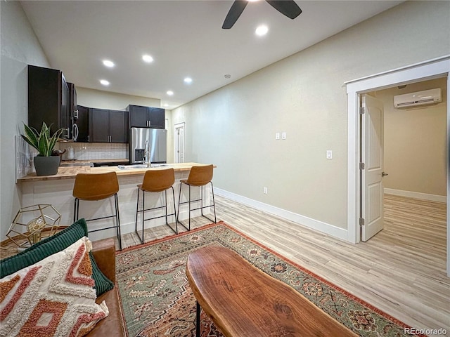 kitchen with a peninsula, light wood-style floors, light countertops, an AC wall unit, and stainless steel fridge with ice dispenser