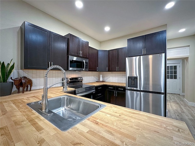 kitchen featuring stainless steel appliances, recessed lighting, wooden counters, backsplash, and a sink