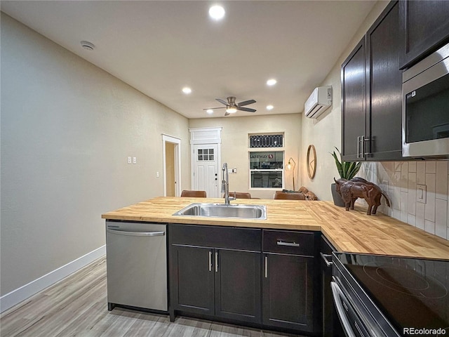 kitchen featuring tasteful backsplash, butcher block countertops, a wall mounted air conditioner, stainless steel appliances, and a sink