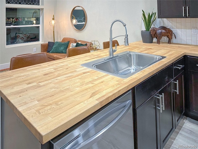 kitchen with stainless steel dishwasher, butcher block counters, backsplash, and a sink