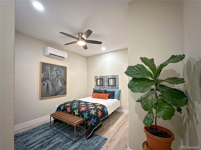 bedroom featuring a wall unit AC, wood finished floors, a ceiling fan, and baseboards