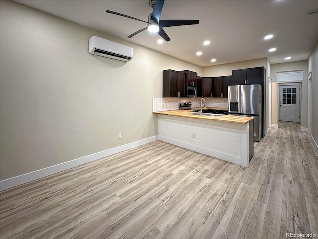 kitchen with tasteful backsplash, butcher block countertops, appliances with stainless steel finishes, an AC wall unit, and a sink