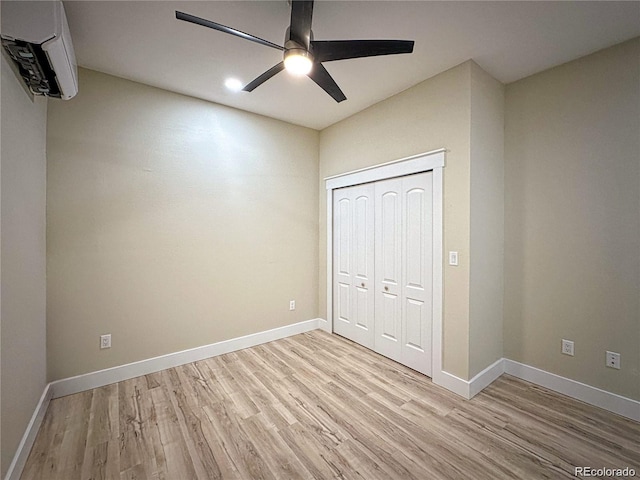 unfurnished bedroom featuring light wood-style floors, baseboards, a closet, and an AC wall unit