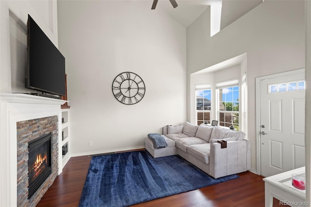 4887 Raven Run, Broomfield, CO 80023 - living room featuring dark wood-style floors, a stone fireplace, a ceiling fan, a towering ceiling, and baseboards