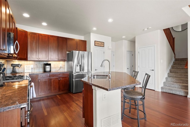4887 Raven Run, Broomfield, CO 80023 - kitchen with appliances with stainless steel finishes, a sink, dark wood finished floors, a breakfast bar, and dark stone counters