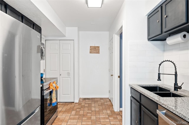 kitchen featuring appliances with stainless steel finishes, sink, light stone counters, and decorative backsplash