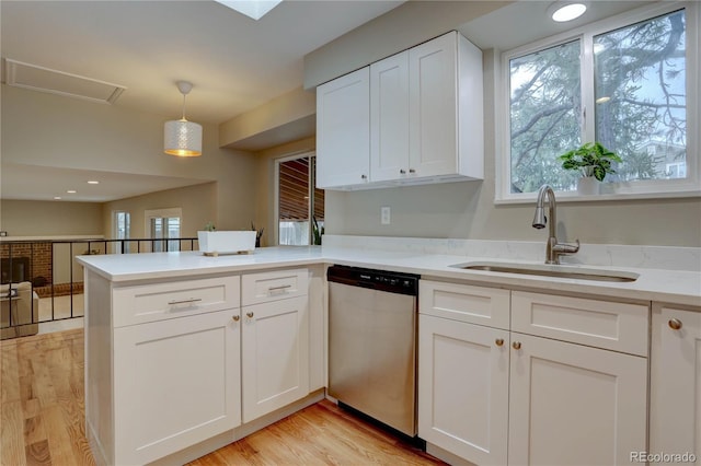 kitchen featuring light wood-style flooring, a sink, stainless steel dishwasher, white cabinetry, and a peninsula