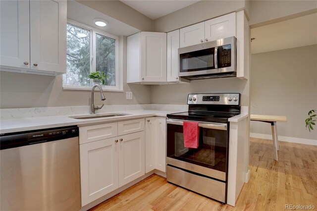 kitchen with light wood finished floors, appliances with stainless steel finishes, light countertops, and a sink