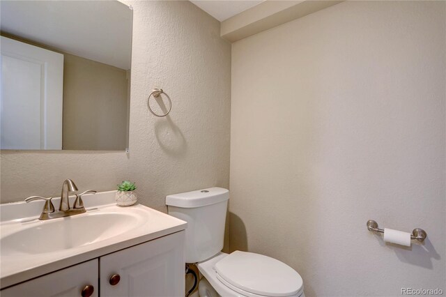 half bath featuring toilet, vanity, and a textured wall