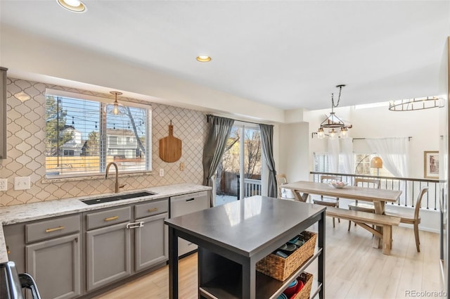 kitchen with dishwasher, hanging light fixtures, light stone counters, sink, and backsplash