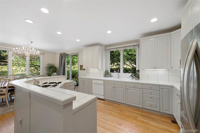 kitchen with white dishwasher, tile counters, stainless steel refrigerator, and white cabinets