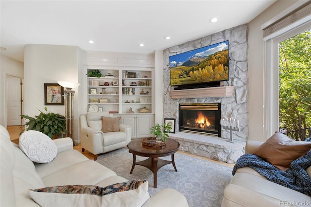 living room with built in shelves, a fireplace, and light wood-type flooring