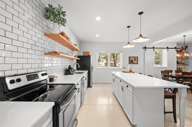 kitchen featuring decorative light fixtures, white cabinetry, backsplash, stainless steel appliances, and a barn door