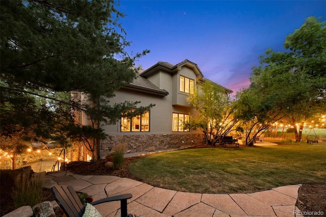 back house at dusk with a patio and a lawn