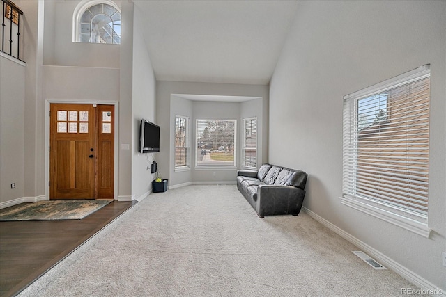 foyer with high vaulted ceiling and dark colored carpet