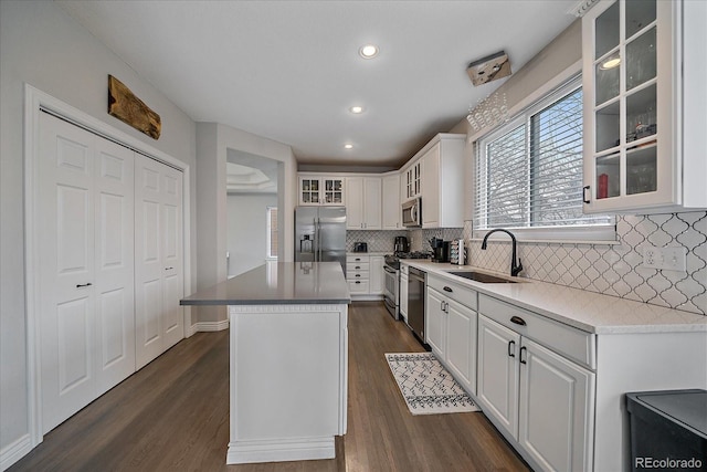 kitchen with a kitchen island, appliances with stainless steel finishes, white cabinetry, sink, and dark wood-type flooring