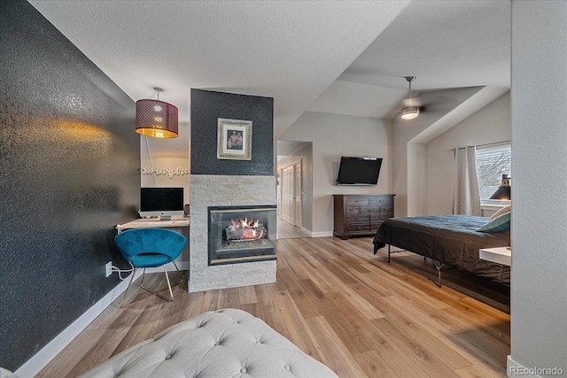 bedroom with a multi sided fireplace, hardwood / wood-style floors, lofted ceiling, ceiling fan, and a textured ceiling