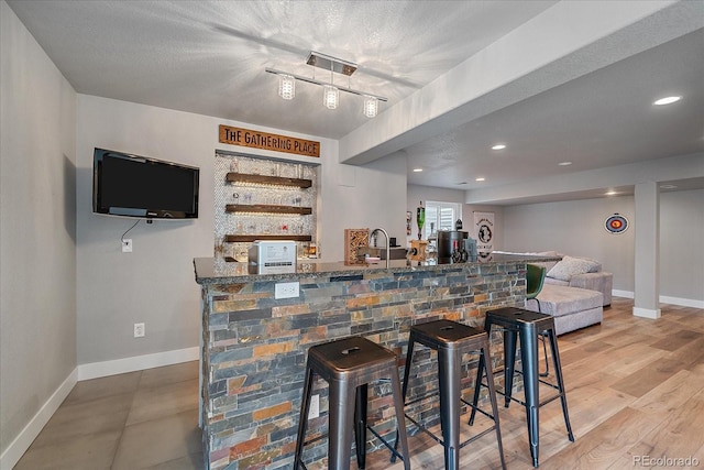 bar featuring dark stone counters, hardwood / wood-style floors, and a textured ceiling