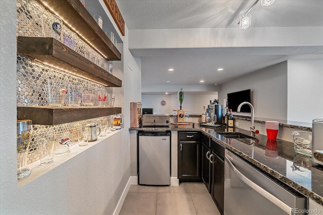 kitchen featuring sink, appliances with stainless steel finishes, a textured ceiling, light tile patterned flooring, and dark stone counters