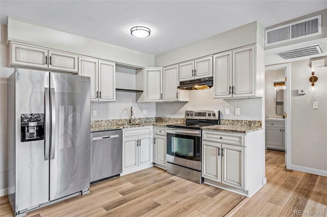 3663 S Sheridan Blvd Unit L6, Denver, CO 80235 - kitchen featuring stainless steel appliances, under cabinet range hood, light wood-style floors, and light stone countertops