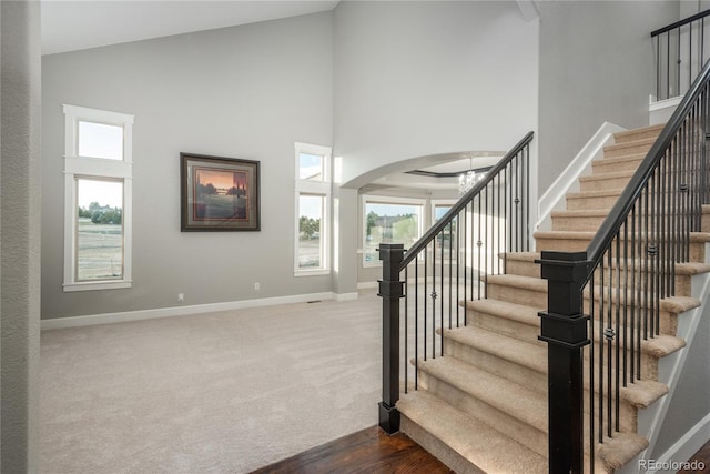 stairs featuring baseboards, arched walkways, a wealth of natural light, and high vaulted ceiling