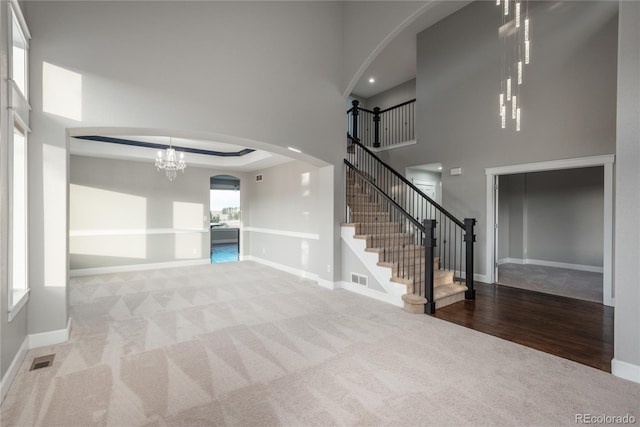 unfurnished living room featuring a notable chandelier, visible vents, arched walkways, and baseboards