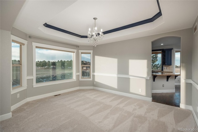 carpeted spare room featuring visible vents, baseboards, arched walkways, a notable chandelier, and a raised ceiling