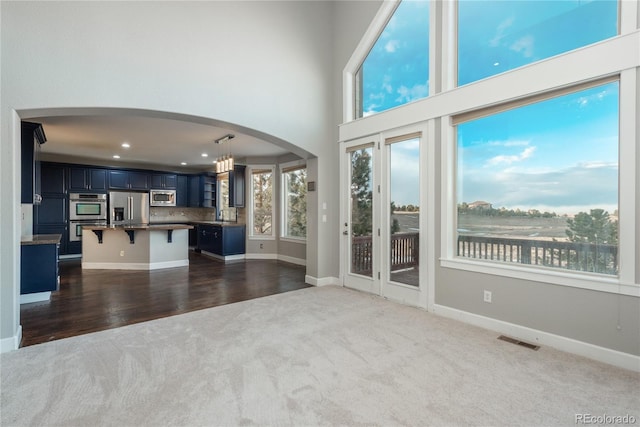 unfurnished living room with visible vents, dark carpet, arched walkways, a high ceiling, and baseboards