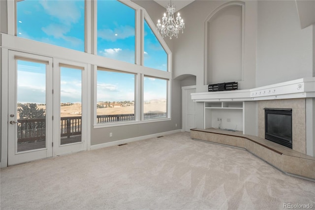 unfurnished living room with carpet, a tiled fireplace, a high ceiling, arched walkways, and a notable chandelier