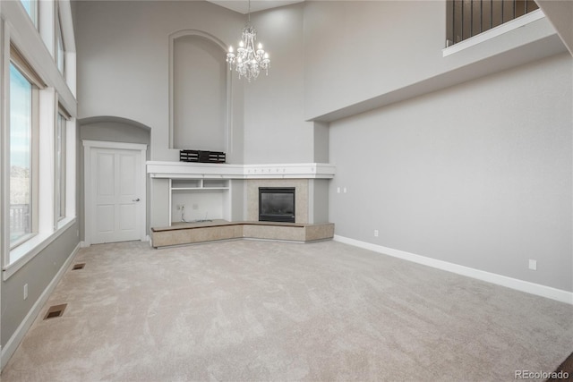 unfurnished living room with an inviting chandelier, a high ceiling, visible vents, and baseboards