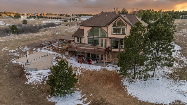 back of house at dusk with a wooden deck and a patio