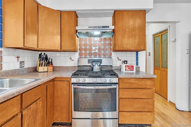 kitchen with brown cabinets, under cabinet range hood, stainless steel range with gas cooktop, and decorative backsplash