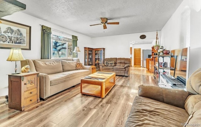 living room with ceiling fan, a textured ceiling, and light wood-type flooring