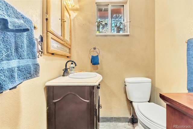 half bathroom featuring toilet, a textured wall, vanity, and baseboards