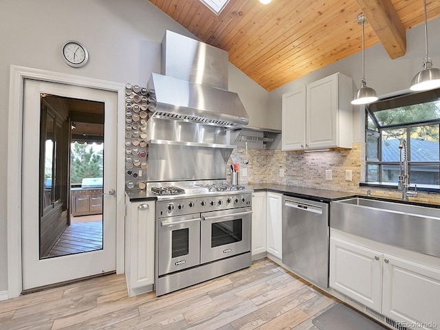 kitchen with wall chimney range hood, white cabinets, stainless steel appliances, and plenty of natural light