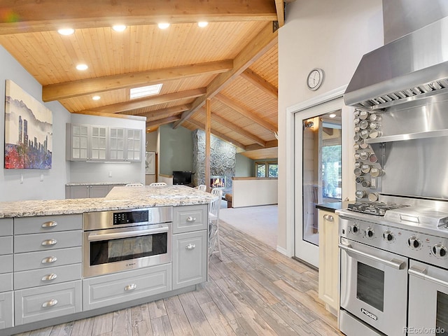 kitchen featuring gray cabinetry, light hardwood / wood-style floors, stainless steel appliances, vaulted ceiling with skylight, and extractor fan