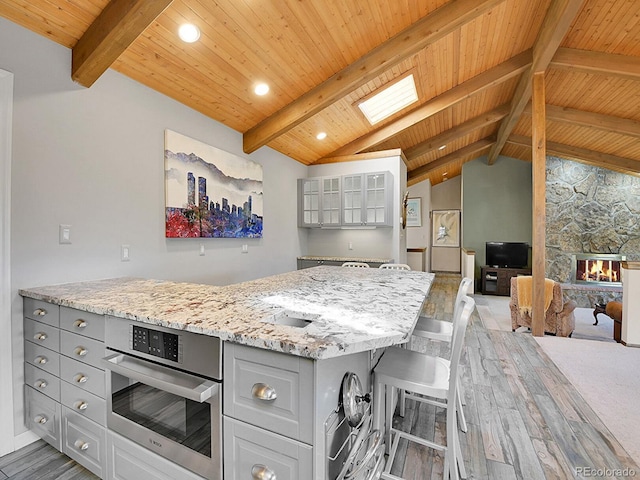 kitchen featuring gray cabinets, light hardwood / wood-style flooring, vaulted ceiling with skylight, and stainless steel oven