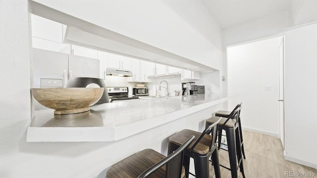 677 Vrain St Unit 15, Denver, CO 80204 - kitchen featuring under cabinet range hood, stainless steel electric range, a kitchen breakfast bar, white cabinetry, and a sink