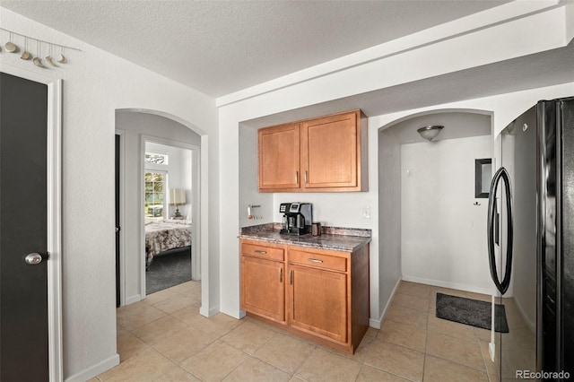 4713 Perth St, Denver, CO 80249 - kitchen featuring freestanding refrigerator, arched walkways, light tile patterned floors, brown cabinets, and a textured ceiling