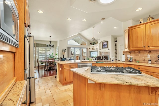 kitchen featuring a kitchen island, appliances with stainless steel finishes, ceiling fan with notable chandelier, backsplash, and kitchen peninsula