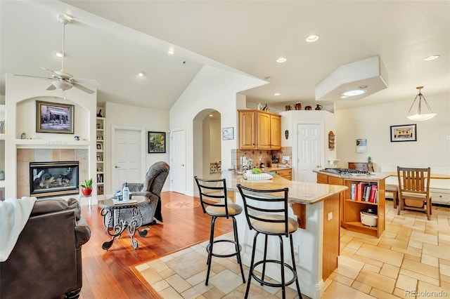 kitchen featuring a breakfast bar area, light hardwood / wood-style flooring, hanging light fixtures, a tiled fireplace, and kitchen peninsula