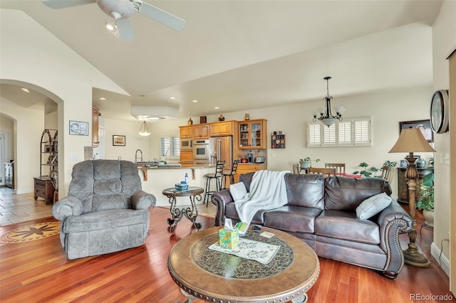 living room featuring high vaulted ceiling, sink, ceiling fan with notable chandelier, and light wood-type flooring