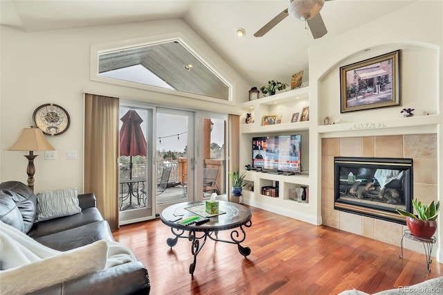 living room with lofted ceiling, ceiling fan, hardwood / wood-style floors, a tiled fireplace, and built in shelves