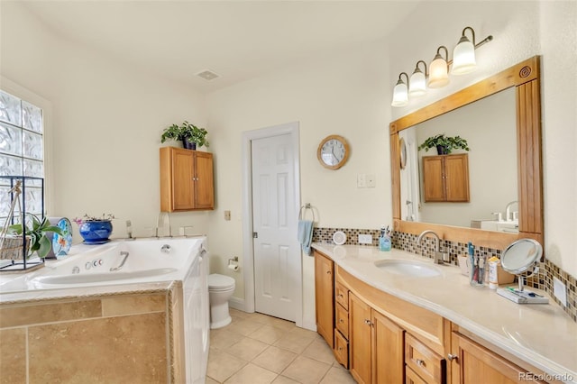 bathroom with tiled bath, backsplash, tile patterned flooring, vanity, and toilet