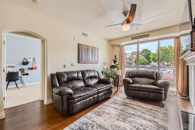 living room with visible vents, arched walkways, baseboards, dark wood-style floors, and ceiling fan