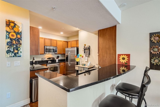 kitchen with brown cabinetry, dark countertops, a breakfast bar area, a peninsula, and stainless steel appliances