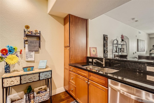 kitchen featuring dark stone counters, dishwasher, brown cabinetry, dark wood-type flooring, and a sink