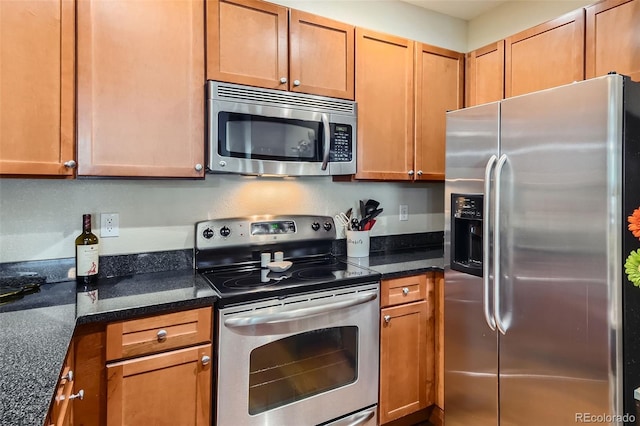 kitchen with brown cabinetry, dark stone counters, and stainless steel appliances