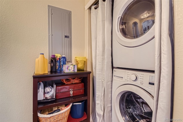 laundry room featuring stacked washer / dryer, laundry area, electric panel, and a textured wall