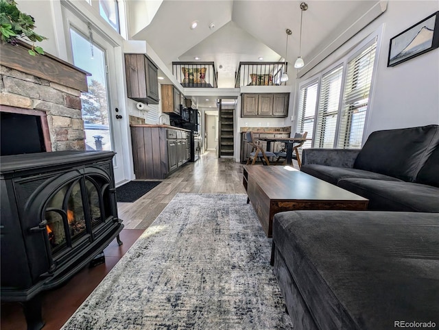 living room with wood-type flooring, high vaulted ceiling, and a wood stove